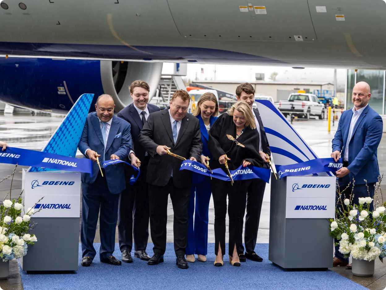 A group of people in business attire cutting a ribbon beside an airplane